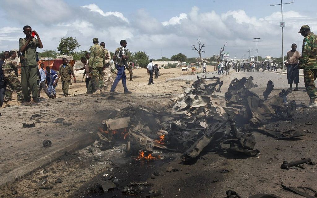 Somali soldiers stand near the wreckage at the scene of a suicide car bomb attack which targeted a convoy of foreign officials, in Mogadishu, Somalia on Wednesday, June 24, 2015. (AP Photo)