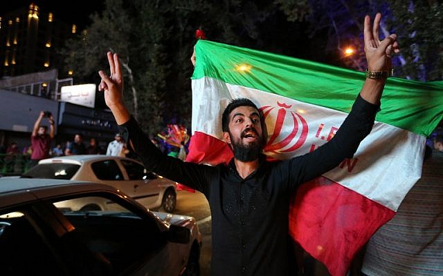 An Iranian man flashes the victory sign as an other holds the Iranian national flag during celebration in northern Tehran on July 14, 2015, after Iran's nuclear negotiating team struck a deal with world powers in Vienna. (AFP PHOTO/ATTA KENARE)