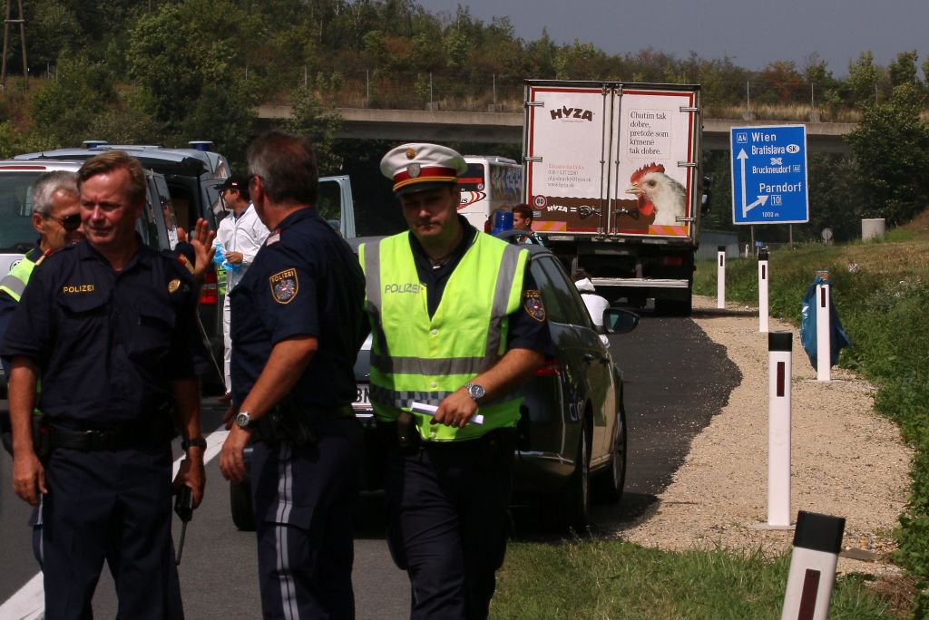 Police stand in fron of a truck parked on the shoulder of the highway A4 near Parndorf south of Vienna, Austria, Thursday, Aug 27, 2015. At least 20 migrants were found dead in the truck parked on the Austrian highway leading from the Hungarian border, police said. (AP Photo/Ronald Zak)