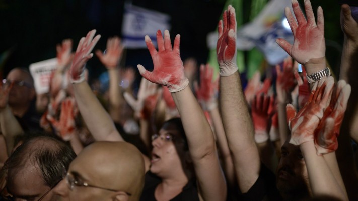 Demonstrators hold up hands painted in red to signify blood while protesting an address by Likud minister Yuval Steinitz at an anti-violence and anti-homophobia rally in Tel Aviv, on August 01, 2015. (Tomer Neuberg/Flash90)