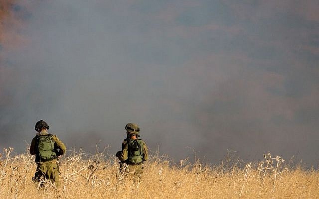IDF soldiers stand near a large brush fire outside Kfar Sold in the Golan Heights sparked by four missiles fired from the Syrian side of the Israeli-Syrian border on August 20, 2015. (Basel Awidat/Flash90)