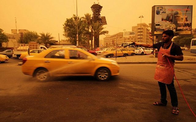 An Iraqi worker sprays water on the tarmac during a sandstorm in the capital Baghdad on September 1, 2015. (AFP Photo/Haidar Mohammed Ali)