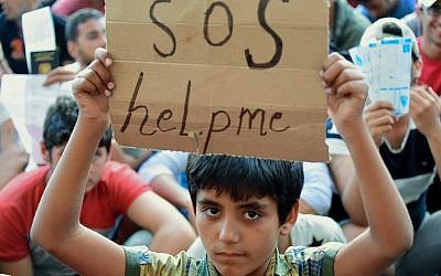 A migrant boy holds a sign reading 'SOS help me' as he sits with other migrants in front of the Keleti (East) railway station in Budapest on September 2, 2015. (AFP PHOTO / ATTILA KISBENEDEK)