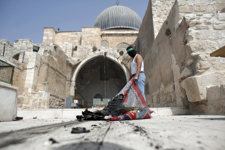 A masked Palestinian wearing a Hamas headband takes a burnt carpet out of Al-Aqsa mosque in Jerusalem's Old City during clashes at the compound on September 13, 2015, just hours before the start of the Jewish new year. (AFP PHOTO/AHMAD GHARABLI)