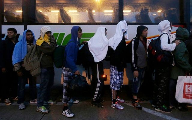 Migrants line up in front of a police bus at the Hungarian-Austrian border in Nickelsdorf, Austria, Saturday, Sept. 5, 2015, where they arrived from Budapest. (AP Photo/Petr David Josek)