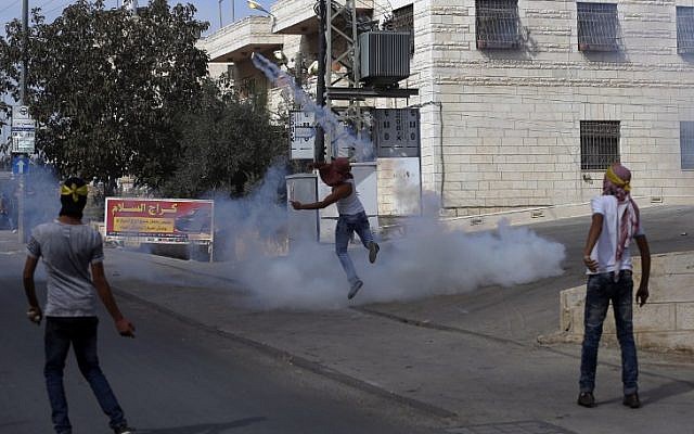 Masked Palestinian youth throw teargas back at Israeli border policemen during clashes in the Palestinian village of al-Ram, between Jerusalem and Ramallah in the West Bank, on October 22, 2015.  (AFP PHOTO/ABBAS MOMANI)
