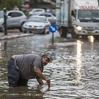 A Israeli man tries to open a sewer drain as water floods a street during a storm in Netanya, north of Tel Aviv, on October 25, 2015. (AFP/Jack Guez)