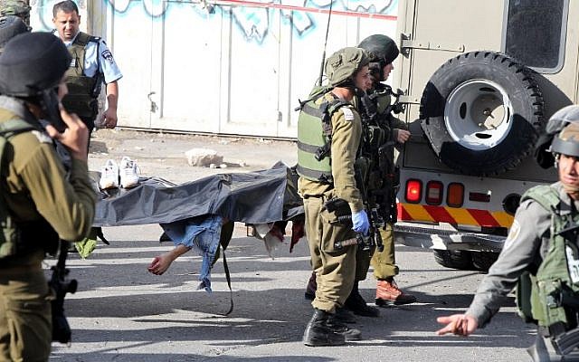 Israeli security forces carry the body of a Palestinian man who stabbed and wounded an IDF soldier before being shot dead by a Border Police officer in Hebron on October 29, 2015. (AFP/HAZEM BADER)