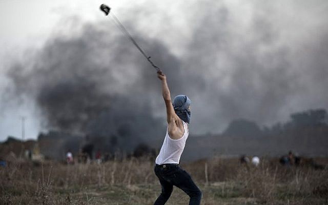 Illustrative: A Palestinian protester uses a slingshot to throw stones towards Israeli soldiers during clashes near the border fence between Israel and the central Gaza Strip on October 15, 2015 (Mohammed Abed/AFP)