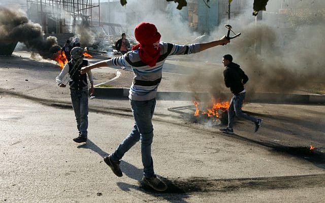 Illustrative: Palestinian protesters throw stones towards Israeli security forces during clashes in the West Bank city of Hebron on November 20, 2015. (AFP/Hazem Bader)