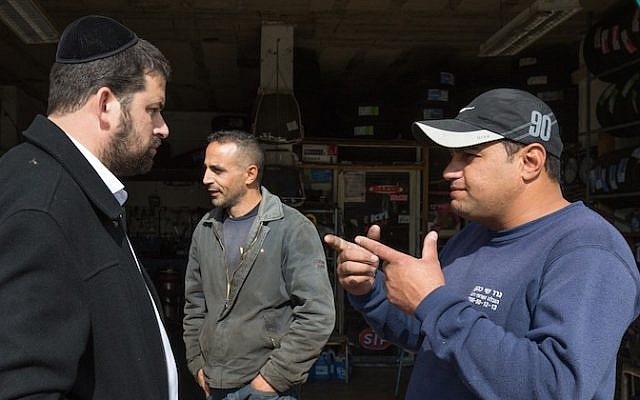 An ultra-Orthodox Jewish man from the Israeli settlement of Beitar Illit seen talking with Arabs as he gets his car washed at the Hussan Junction Palestinian-owned car wash in the West Bank, on November 11, 2015. (Nati Shohat/Flash90)