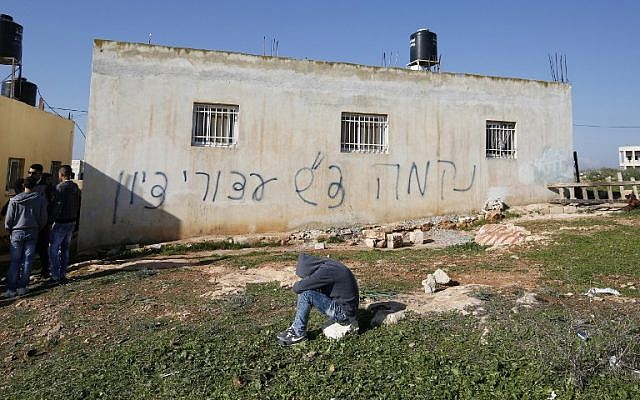 Palestinians gather next to a house sprayed with graffiti reading in Hebrew: 'revenge' and 'hello from the prisoners of Zion,' in the West Bank village of Beitillu on December 22, 2015.(AFP PHOTO/ABBAS MOMANI)