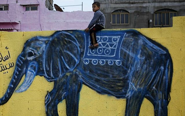 In this Tuesday, Dec. 15, 2015 photo, a Palestinian boy sits atop a wall with an elephant painting in the Shati refugee camp in Gaza City. (AP Photo/Hatem Moussa)