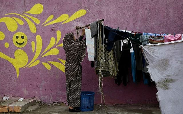 In this Saturday, Dec. 19, 2015 photo, a Palestinian woman hangs laundry in front of her painted house in the Shati Refugee Camp in Gaza City. (AP Photo/Hatem Moussa)