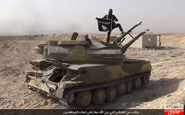 In this file photo released on Aug. 5, 2015, by the Rased News Network a Facebook page affiliated with Islamic State militants, an Islamic State militant holds the group's flag as he stands on a tank they captured from Syrian government forces, in the town of Qaryatain southwest of Palmyra, central Syria. (Rased News Network via AP, File)