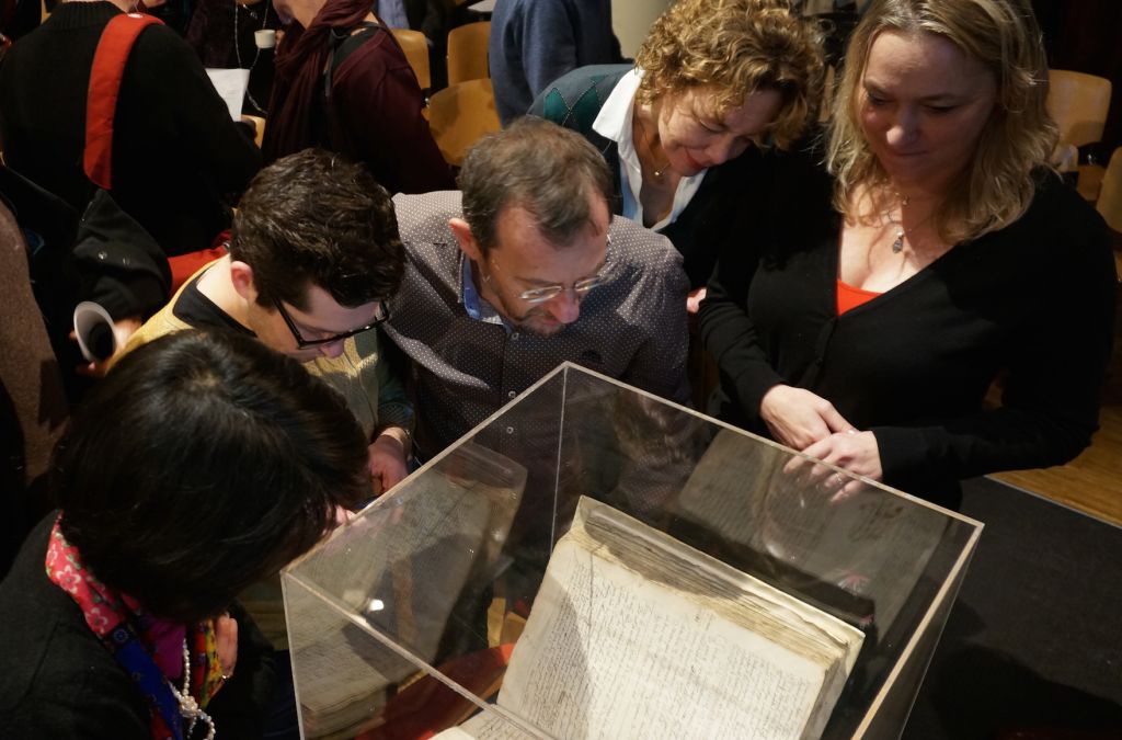 Attendees at an Amsterdam symposium on whether to lift the ancient order of excommunication against the philosopher Baruch Spinoza examining a copy of the original writ against him, December 6, 2015 (Cnaan Liphshiz/JTA)