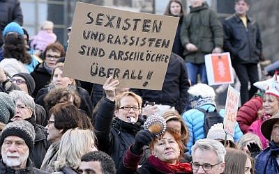 A woman holds up a sign reading "Sexists and racists are assholes-everywhere" while taking part in a demonstration against violence against women in front of the cathedral in Cologne, western Germany, on January 9, 2015 (Roberto Pfeil/AFP)