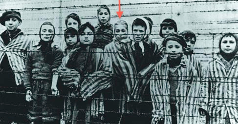 Marta Wise (center with red arrow) stands with a group of children behind the Auschwitz barbed wire. (courtesy)