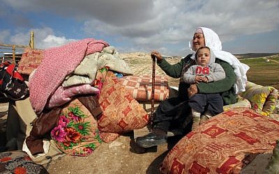 A Palestinian woman sits holding a child next to items salvaged from the remains of their home after it was demolished by Israeli bulldozers in a disputed military zone in the area of Musafir Jenbah, which includes several villages, south of the West Bank town of Hebron on February 2, 2016. / AFP / HAZEM BADER 