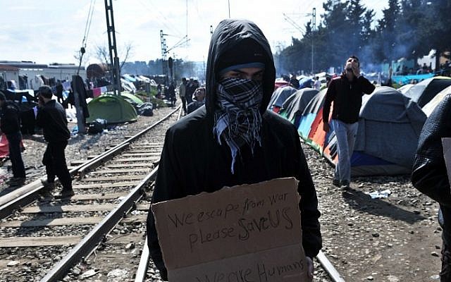 A migrant holds a placard reading "We escape from war, please save us, we are humans" in a makeshift camp at the Greek-Macedonian border, near the Greek village of Idomeni, on March 18, 2016. (Sakis Mitrolidis/AFP)