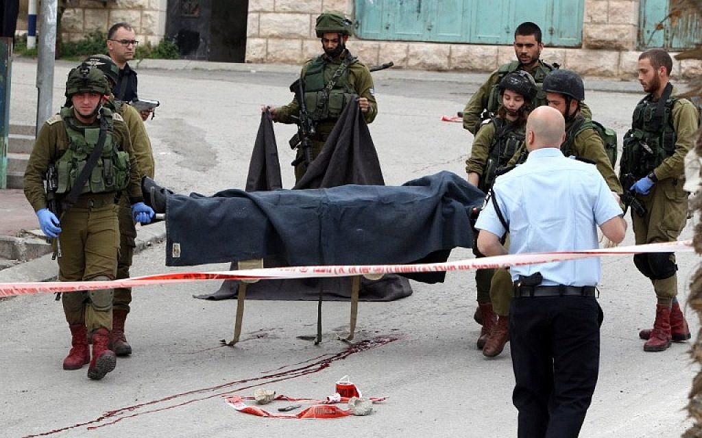 Israeli soldiers carry the body of one of the two Palestinians who were killed after wounding an Israeli soldier in a knife attack before being shot dead by troops at the entrance to the Jewish enclave of Tal Rumeida in the city center of the West Bank town of Hebron, March 24, 2016. (AFP/Hazem Bader)