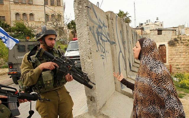 A Palestinian woman speaks with an Israeli soldier at the scene of an attack in which two Palestinians wounded an Israeli soldier in a knife attack before being shot dead by troops in the city center of the West Bank town of Hebron on March 24, 2016. (AFP/Hazem Bader)