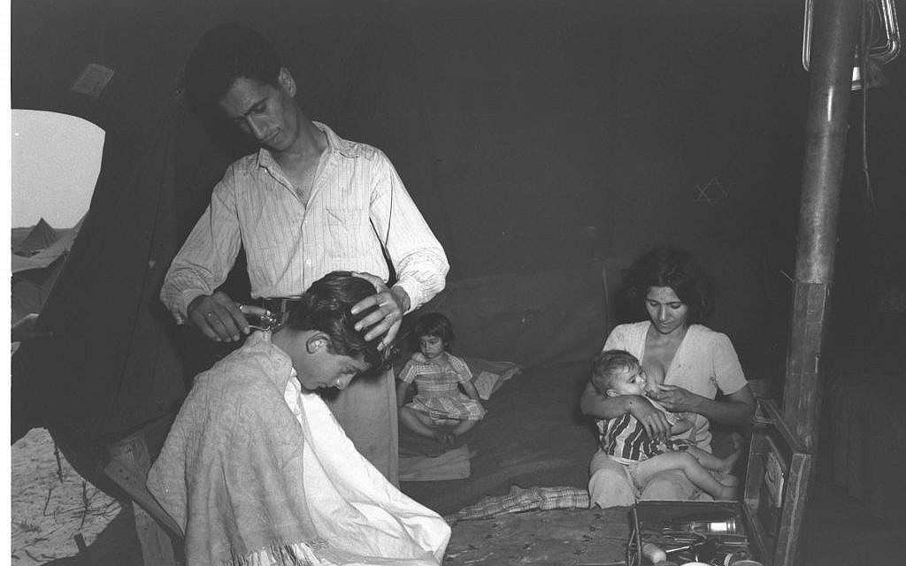 Barber Rachamim Azar, a new immigrant from Baghdad, carries out his trade in the tent he shares with his wife and two children at a maabara (immigrant camp) in central Israel in summer 1951. He told a Government Press Office photographer that he intended to move to a kibbutz  (Teddy Brauner, GPO)