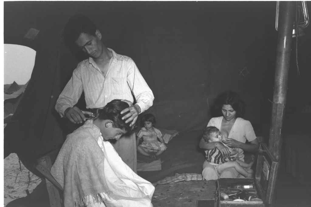 Barber Rachamim Azar, a new immigrant from Baghdad, carries out his trade in the tent he shares with his wife and two children at a maabara (immigrant camp) in central Israel in summer 1951. He told a Government Press Office photographer that he intended to move to a kibbutz (Teddy Brauner, GPO)