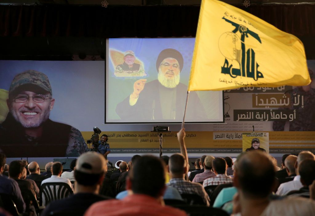 A Hezbollah supporter waves his group's flag, as Hezbollah leader Hassan Nasrallah, center, speaks via a video link, in the southern suburb of Beirut, Lebanon, Friday, June 24, 2016. Nasrallah said the Lebanese Shiite militant group will send more fighters to Syria's Aleppo province, where pro-government forces are battling Syrian rebels on several fronts. (AP Photo/Hussein Malla)