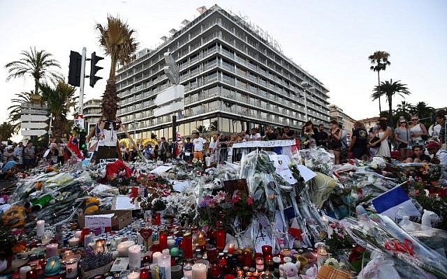 This photo taken on July 16, 2016 in front of Le Meridien hotel in Nice, southern France, shows people gathering around flowers and candles placed in the road for victims of the deadly Bastille Day attack.(AFP PHOTO / ANNE-CHRISTINE POUJOULAT)