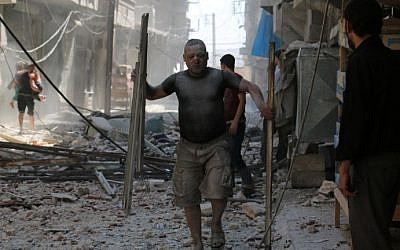 A Syrian man covered with dust carries pieces of metal on a street cluttered with rubble following a reported air strike on the rebel-held neighborhood of Sakhur in the northern city of Aleppo, on August 15, 2016. (AFP PHOTO/AMEER ALHALBI)