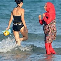 Women, one, wearing a 'burkini,' a full-body swimsuit designed for Muslim women, walk in the water on Ghar El Melh beach near Bizerte, north-east of the capital Tunis, August 16, 2016.  (AFP/FETHI BELAID)
