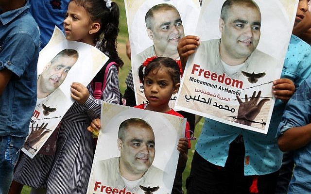 Palestinian children hold posters of Muhammad Halabi, left, the Gaza director of World Vision, a major US-based Christian NGO, during a protest to support him at Rafah town in the southern Gaza Strip August 29, 2016. (AFP/SAID KHATIB)