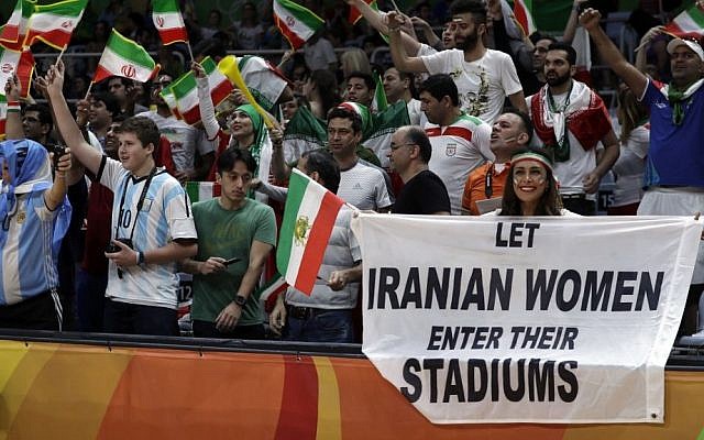Fans cheer and wave the flag of Iran as Darya Safai, right, holds a large sign protesting the fact that women have not been allowed to attend volleyball matches in Iran during a men's preliminary volleyball match between Egypt and Iran at the 2016 Summer Olympics in Rio de Janeiro, Brazil, Saturday, August 13, 2016. (AP/Jeff Roberson)
