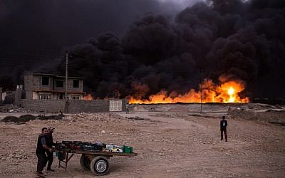 Iraqi villagers walk past a fire from oil that has been set ablaze in the Qayyarah area, some 60 kilometers south of Mosul, on October 19, 2016. ( AFP PHOTO / YASIN AKGUL)