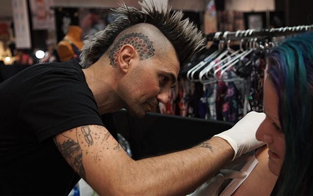 Shay Daudi, producer of Israel's Tattoo Convention, pierces a client at the annual event in Tel Aviv. October 7, 2016. (Luke Tress/Times of Israel)