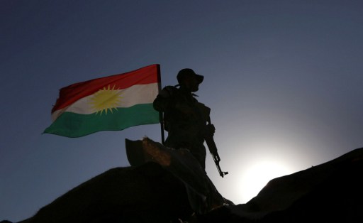 An Iraqi Kurdish Peshmerga fighter, next to a Kurdish flag, holds a position in Sheikh Ali village near the town of Bashiqa, some 25 kilometers north east of Mosul, on November 6, 2016 during an operation against IS jihadists to retake the main hub city. (AFP PHOTO / SAFIN HAMED)