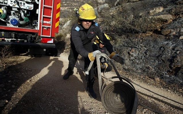 An Israeli firefighter unloads hose as they battle a fire in the village of Nataf close to Jerusalem, as it continues to spread in the area, on November 26, 2016. (AFP PHOTO / AHMAD GHARABLI)