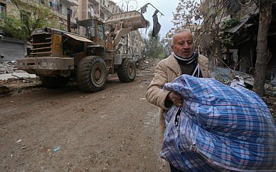 A Syrian man walks past a bulldozer removing rubble from a road as Syrian pro-government forces re-open a street in Aleppo's old city that was formerly barricaded, dividing the government-held and rebel-held areas, on December 17, 2016. 
(Youssef Karwashan/AFP)
