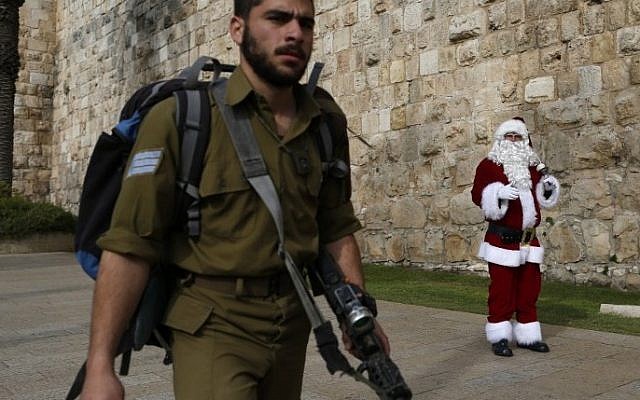 An Israeli soldier walks past a Palestinian man dressed up as Santa Claus outside Jaffa Gate in Jerusalem's Old City, on December 23, 2016. (AFP/Ahmad Gharabli)