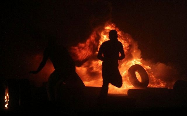 Illustrative photo of Palestinian men burning tires during clashes with Israeli border police at the Qalandiya checkpoint, between Jerusalem and Ramallah, late on July 24, 2014. (Issam Rimawi/Flash90)