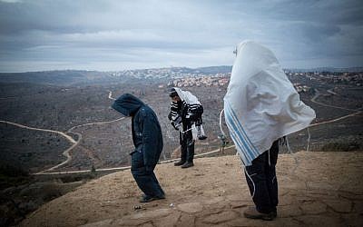 Jewish men pray early in the morning on the hill overlooking Ofra in the Jewish outpost of Amona in the West Bank, on December 18, 2016. (Miriam Alster/Flash90 