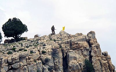 In this Saturday, May 9, 2015 file photo, a Hezbollah fighter stands on a hill next to the group's yellow flag in the fields of the Syrian town of Assal al-Ward in the mountainous region of Qalamoun, Syria. (AP Photo/Bassem Mroue, File)