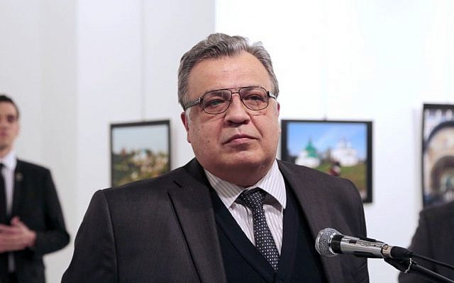 Andrei Karlov, the Russian ambassador to Turkey, pauses during a speech at a photo exhibition, moments before a gunman, identified as Mevlut Mert Altintas, seen standing in the background, left, fatally shoots him in Ankara, December 19, 2016 (AP/Burhan Ozbilici)