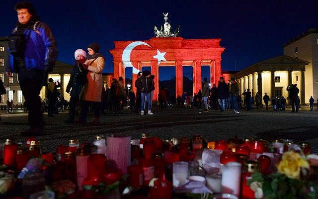 In a tribute to the victims of the Reina night club attack in Istanbul, people leave flowers and candles at a makeshift memorial in front of Berlin's landmark Brandenburg Gate, illuminated in the colors of the Turkish flag, in Berlin, January 2, 2017. (AFP/dpa/Maurizio Gambarini)