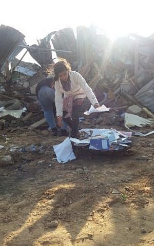 A girl picks out what seems to be textbooks and notebooks for school out of the rubble of her home in Umm al-Hiran on January 18, 2017. (Credit: Dov Lieber / Times of Israel)