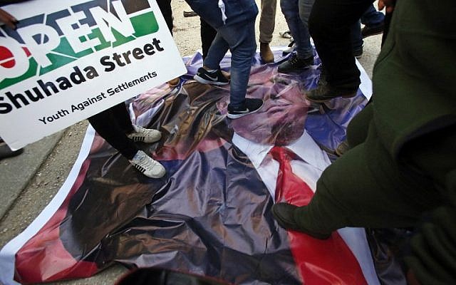 Palestinian demonstrators stand on a poster of US President Donald Trump as they protest against his support of Israel and demand for the Israeli army to re-open Shuhada Street near a Jewish settler enclave in the heart of the flashpoint West Bank city of Hebron, which it has largely closed off to Palestinians, on February 24, 2017. (AFP/Hazem Bader)