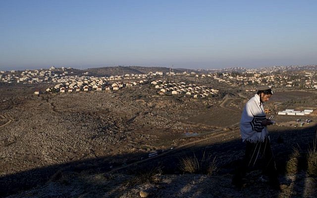 A man praying at the illegal outpost of Amona, with a view of West Bank settlements, on February 2, 2017. (Yonatan Sindel/Flash90)