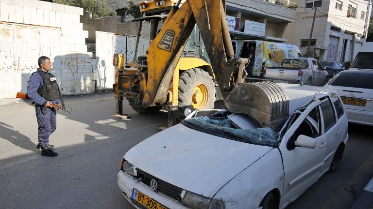 A bulldozer smashes its shovel into a car with an Israeli license plate in the West Bank village of al-Ram on March 6, 2017. (AFP Photo/Abbas Momani)