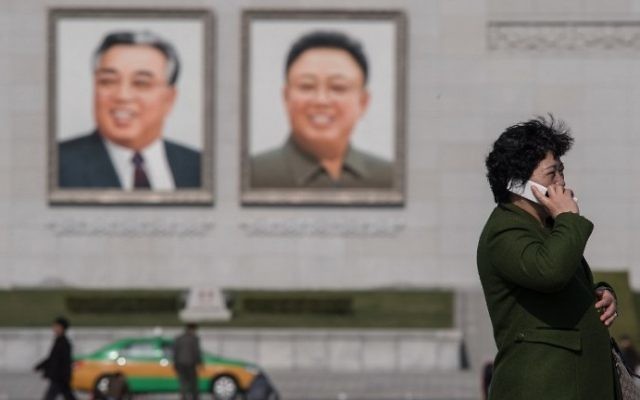 In a photo taken on April 9, 2017 a woman uses a mobile phone as a taxi passes the portraits of late North Korean leaders Kim Il-Sung (L) and Kim Jong-il (R) in Pyongyang. AFP/Ed JONES)